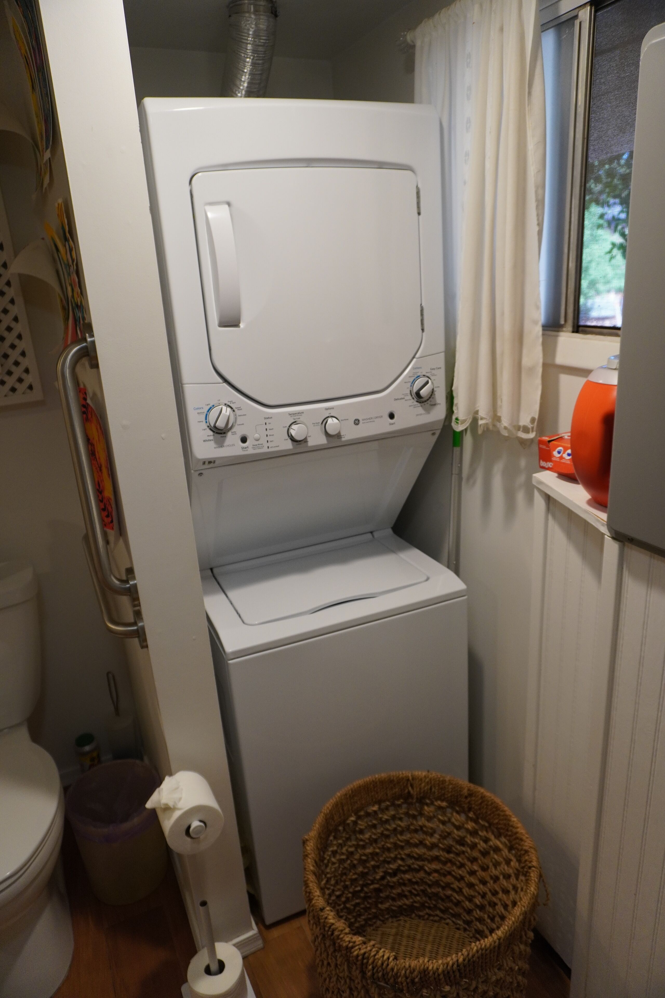 A compact laundry area with a front-loading washing machine, a wicker basket, and a toilet.