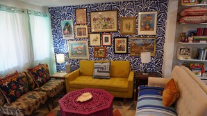 Una sala de estar con papel tapiz estampado, un sofá amarillo, un sofá a rayas y una mesa rosa.