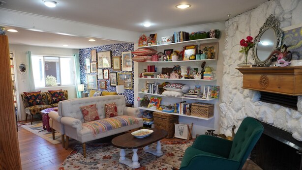 Una sala de estar acogedora con un sofá, un sillón y una mesa de centro, rodeada de estanterías con diversos objetos decorativos y libros.