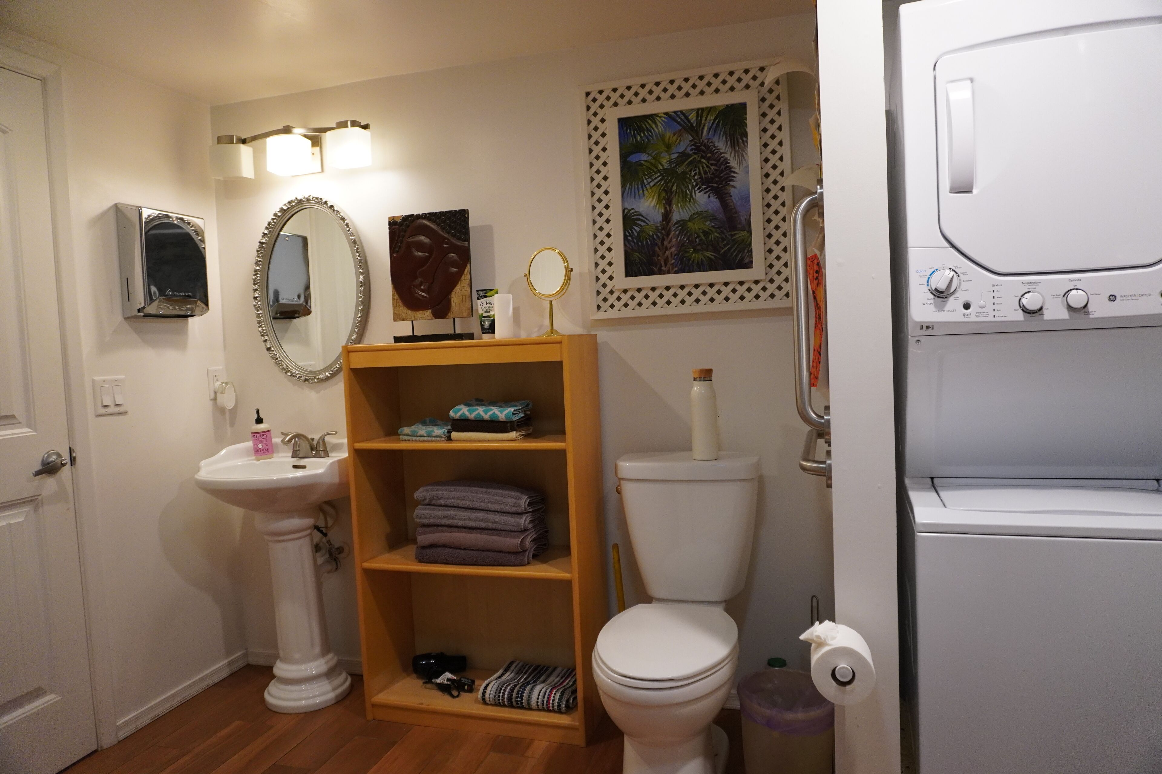 A bathroom with a pedestal sink, toilet, and a shelf with folded towels.