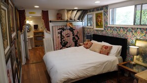 Un dormitorio con una cama grande, una mesita de noche, un espejo, una ventana y una pared cubierta de papel tapiz floral.