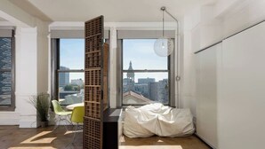 Una stanza moderna con ampie finestre, un pannello in legno, una sedia verde e un pouf bianco.