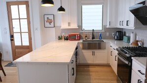 A modern kitchen with white cabinets, a large island, a red microwave, and a gas stove. - Parkside Central Retreat (Houston)