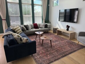 A living room with a sofa, a coffee table, a TV, and a patterned rug. - Parkside Central Retreat (Houston)