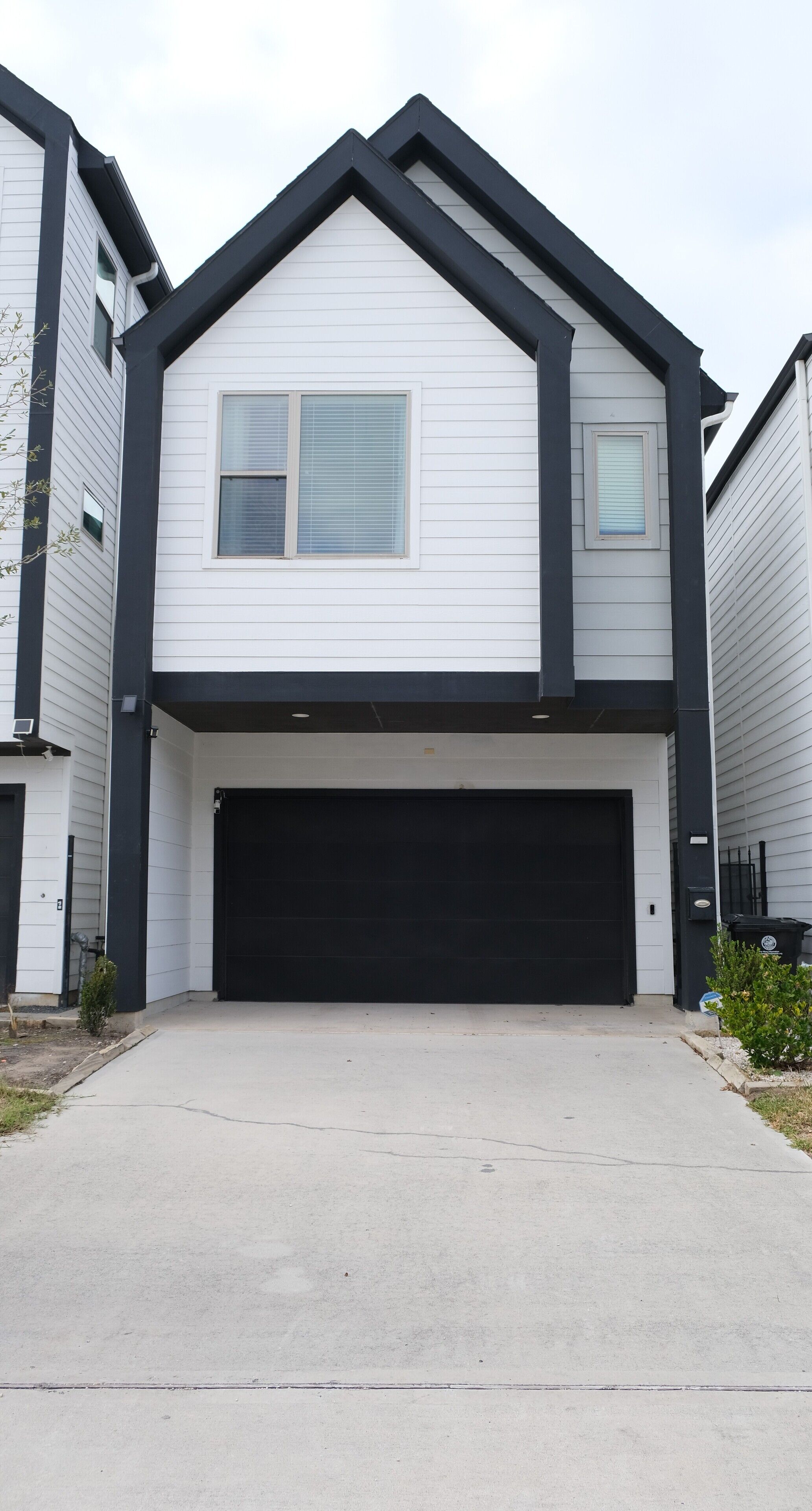 A two-story house with a black garage door, white siding, and a gable roof.