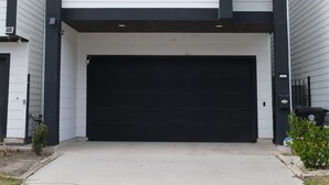 A two-story house with a black garage door, white siding, and a gable roof. - Parkside Central Retreat (Houston)