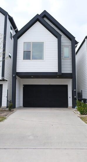 A two-story house with a black garage door, white siding, and a gable roof. - Parkside Central Retreat (Houston)