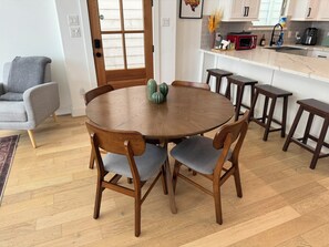 A round wooden dining table with six chairs, a kitchen area with white cabinets, a red microwave, and a sink. - Parkside Central Retreat (Houston)