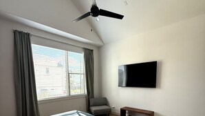A bedroom with a bed, a ceiling fan, a TV, a window with curtains, and a bench. - Parkside Central Retreat (Houston)