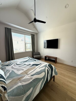Un dormitorio con cama, ventilador de techo, televisión, ventana con cortinas y una banca.
