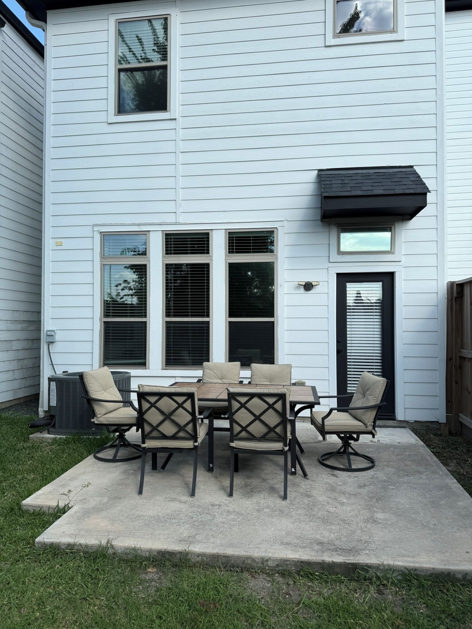 Un patio con una mesa, sillas, una puerta negra y una ventana con persianas.