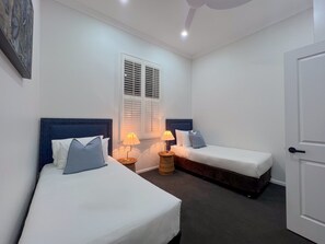 Habitación de hotel con dos camas individuales, una ventana con persianas, una puerta y una pequeña mesa con lámparas.