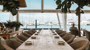 A dining table set for a meal with wicker chairs, a view of boats at a marina, and potted plants. - 4BDR Queenslander with Pool Near Manly Esplanade (Manly)