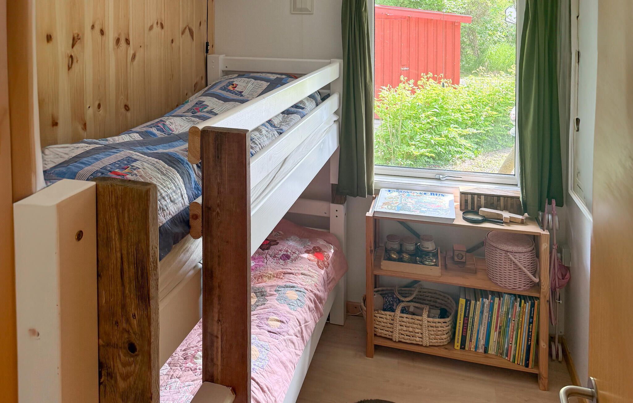 Une chambre de dortoir avec deux lits superposés, un bureau en bois avec une carte et des livres, et une fenêtre donnant sur un paysage verdoyant.
