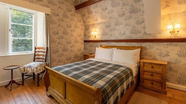 A traditional bedroom with a wooden bed, a small bedside table, a chair, and a window with curtains. - St Andrews House (Fort William)