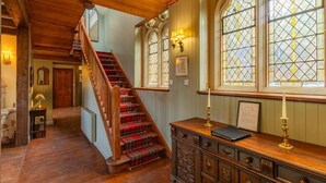A wooden staircase with red plaid carpeting, a wooden dresser with a lamp, and a window with stained glass. - St Andrews House (Fort William)