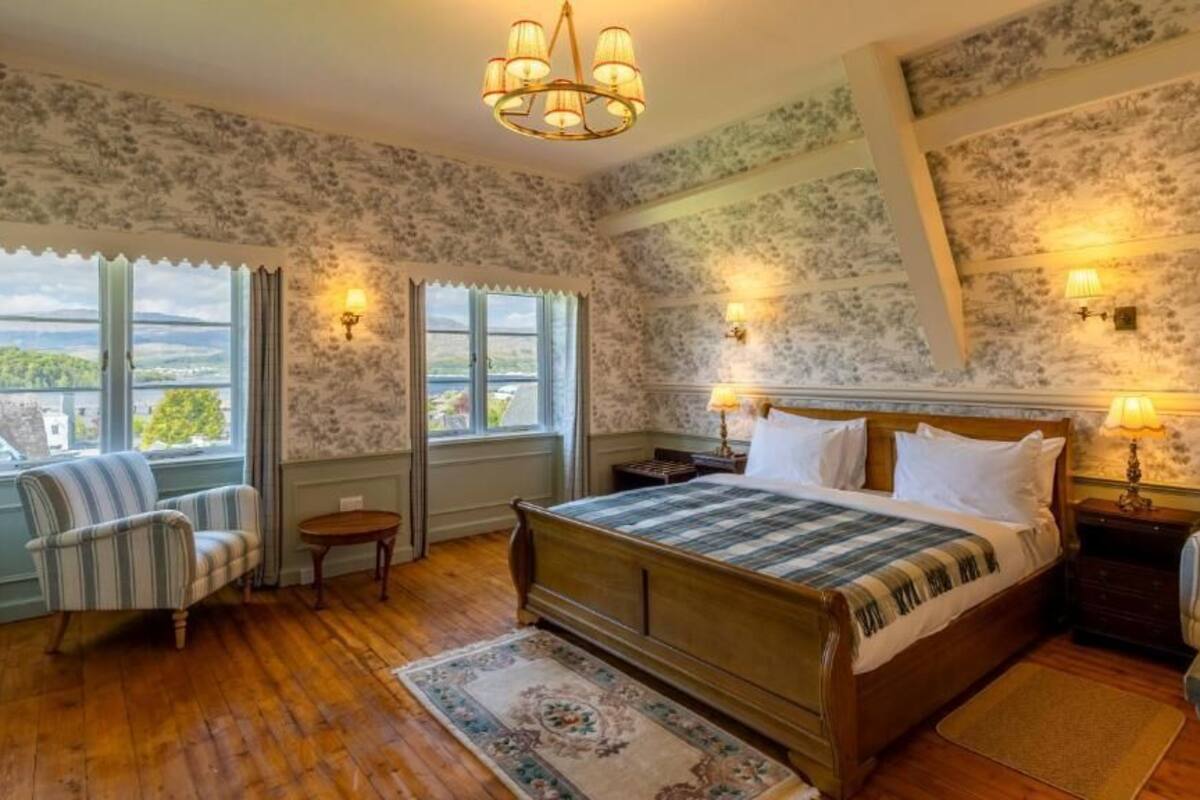 A bedroom with a large bed, two bedside tables, a chair, and a window with curtains.