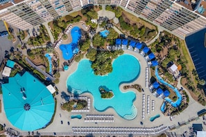 Eine Vogelperspektive zeigt einen luxuriösen Urlaubsort mit mehreren Schwimmbecken, Liegestühlen und Palmen.