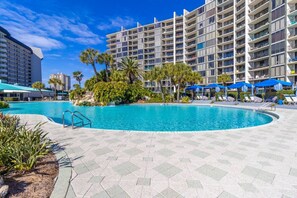 Een hotel met een zwembad, palmbomen en blauwe parasols.