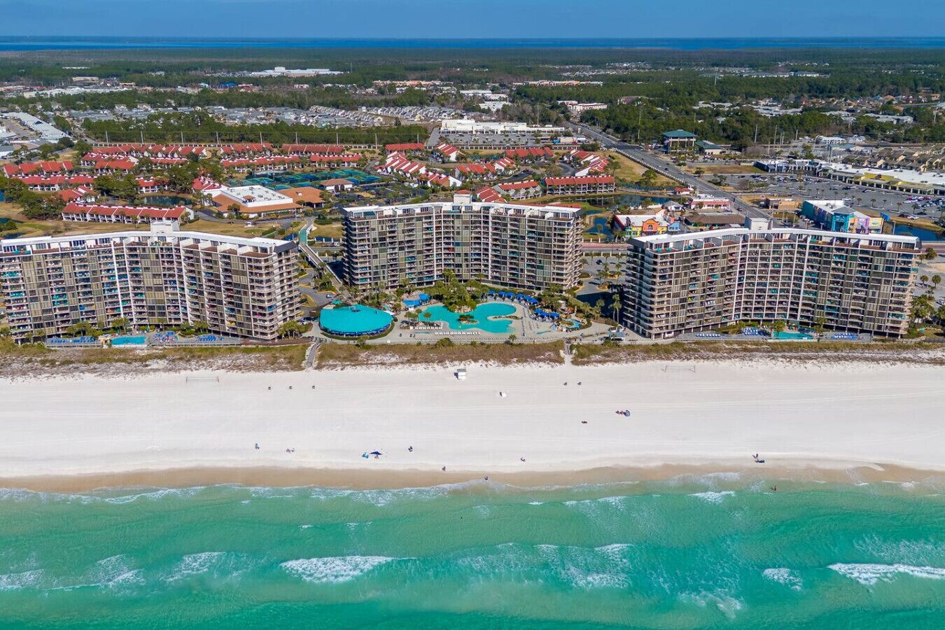Un hotel costero con varios edificios altos, una playa y un amplio complejo de piscinas.