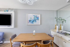 Een moderne eetruimte met een houten tafel en stoelen, een flatscreen televisie aan de muur en een schilderij met abstracte kunst boven de tafel.