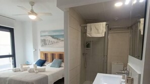 Quarto de hotel moderno com cama, chuveiro e banheiro com pia e espelho.