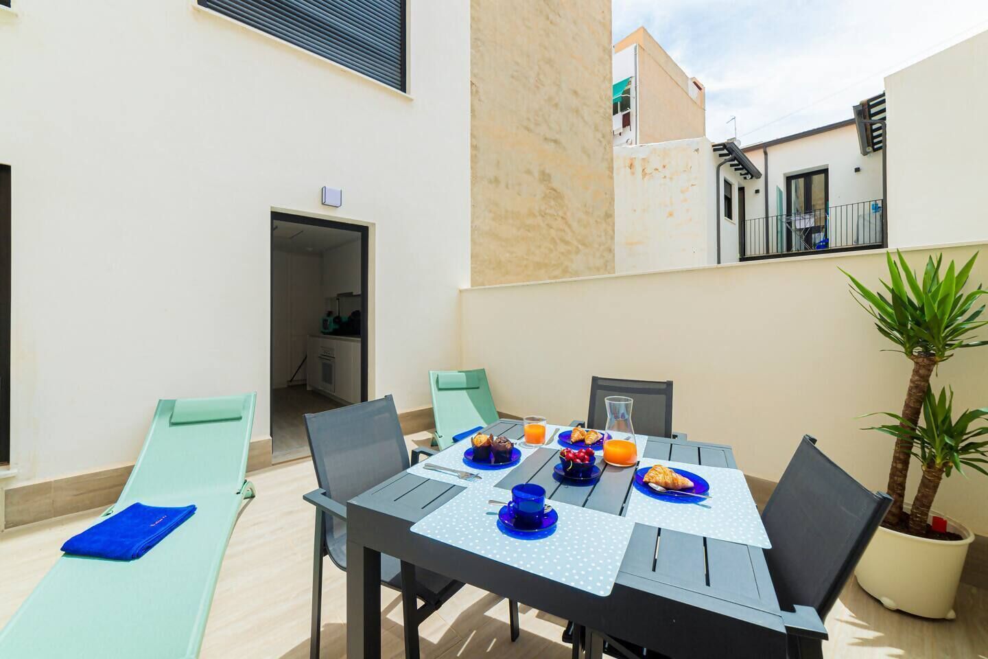 Un coin repas avec une table dressée pour quatre personnes, entourée de chaises, d’un ordinateur portable et d’une plante en pot.