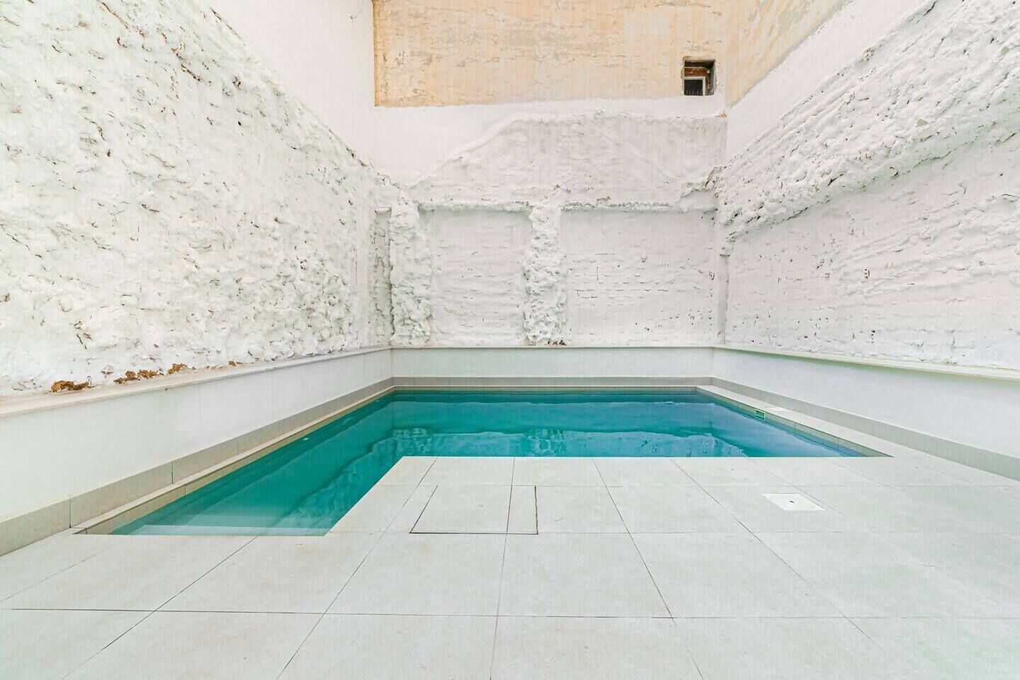 A swimming pool with white textured walls and a tiled floor.