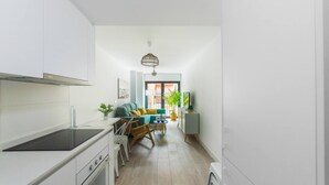 A modern kitchen with white cabinets, a black countertop, and a built-in oven. There is a dining area with a wooden table and chairs, and a sofa with cushions. A potted plant is on the dining table. - Costa ap. 2nd floor shared heated pool (Alicante/Alacant)