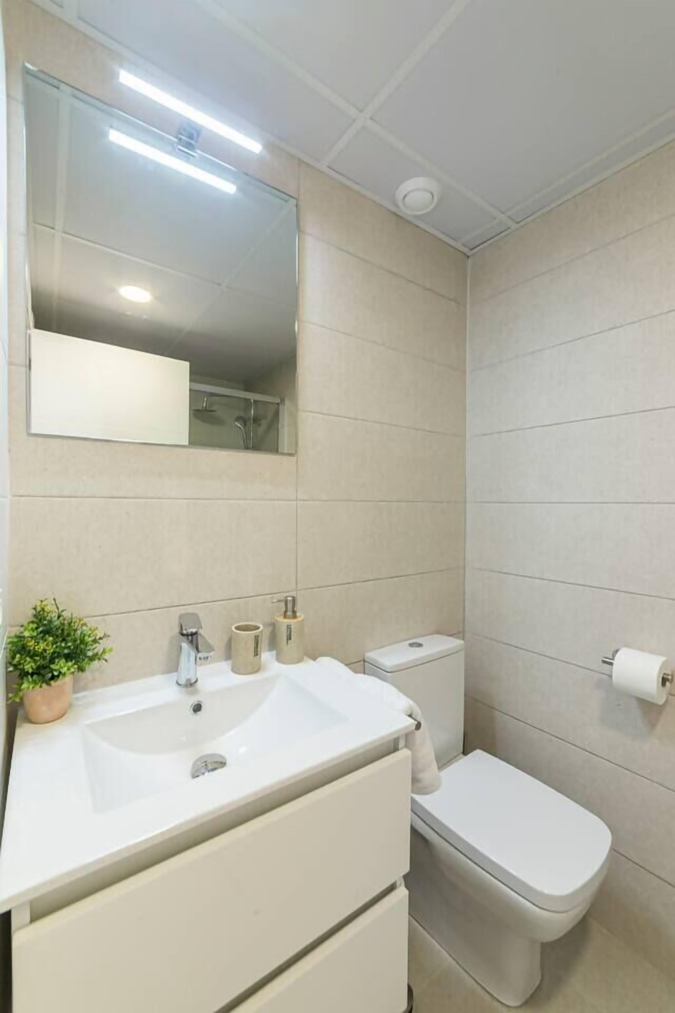 A modern bathroom with a white sink, mirror, and toilet.