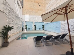 Una piscina interior con suelo de baldosas, sillones de descanso y plantas en macetas.