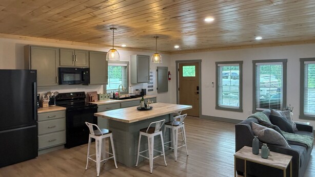Een moderne keuken met houten plafond, een centraal eiland met barstoelen, een koelkast en een magnetron.