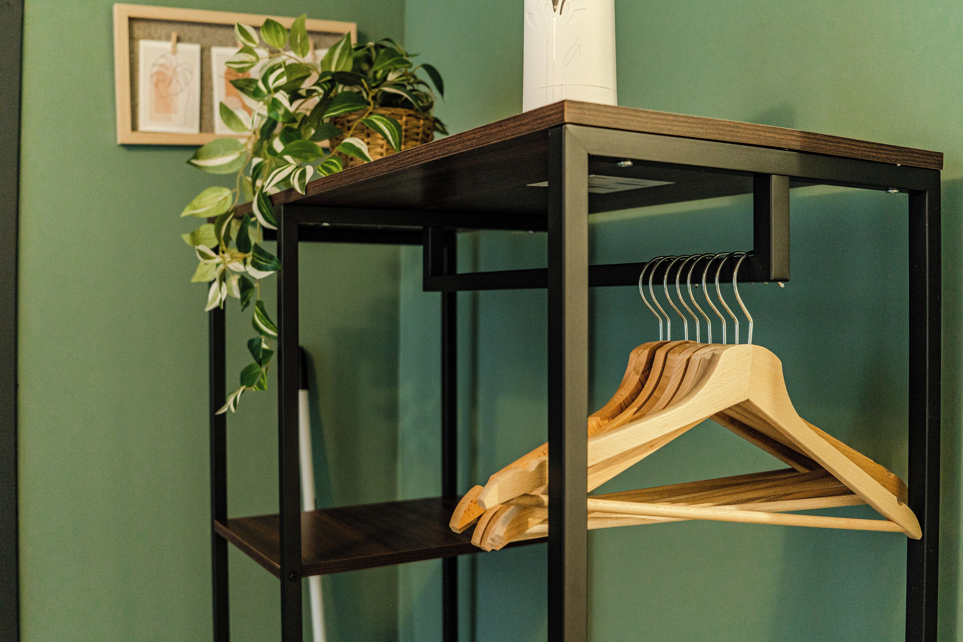 Un porte-cintres en bois est posé sur une table en métal noir, avec un mur vert en arrière-plan.