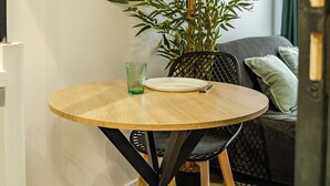 A round wooden table with a black metal base, a glass, and a white plate. A bamboo plant is beside the table. - CosyEmerald (Cambrai)