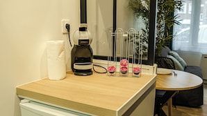 A kitchenette with a coffee maker, a roll of paper towels, and a glass jar with a red lid on the counter. - CosyEmerald (Cambrai)