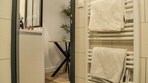A bathroom with a white towel rack, a mirror, and a small table with a plant. - CosyEmerald (Cambrai)