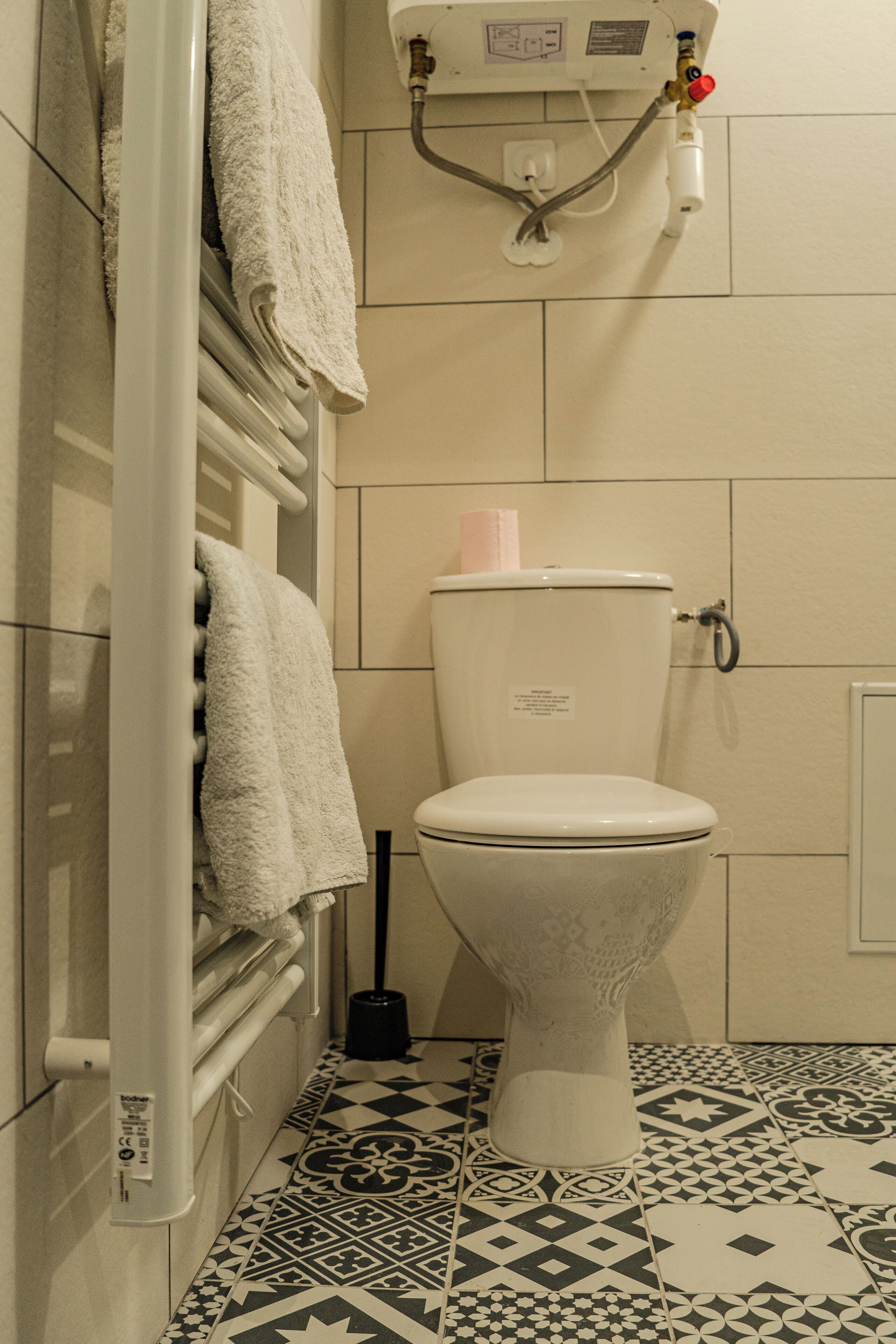 A bathroom with a toilet, a towel rack with towels, a toilet paper holder, and a floor with patterned tiles.