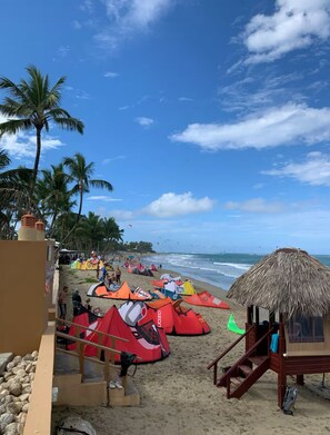 A beach with multiple colorful tents and a thatched-roof hut. - Beachfront Penthouse in Cabarete beach (Cabarete)