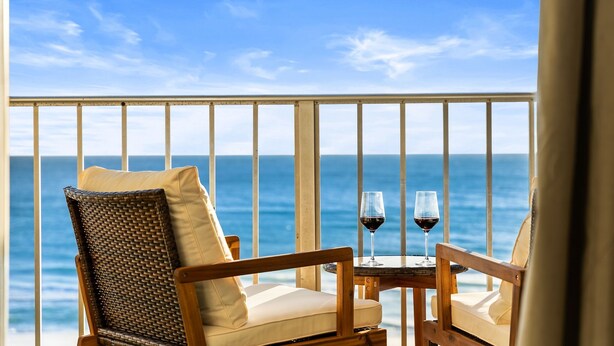 A balcony with two wicker chairs and a small table, each with a glass of red wine. - Brand New Luxury | Sunset Balcony | 3 Pools (panama city beach)