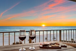 Due bicchieri di vino su un tavolo di legno con vista sul tramonto sull'oceano.