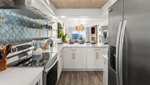 A modern kitchen with white cabinetry, stainless steel appliances, and a wooden ceiling. - Brand New Luxury | Sunset Balcony | 3 Pools (panama city beach)