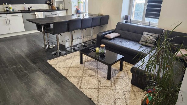 A modern living room with a black sofa, a coffee table, and a bar area with stools. - Apartment morteau center (Morteau)