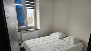 A bedroom with a bed, white bedding, a window with blinds, and a radiator. - Apartment morteau center (Morteau)