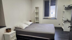 A bedroom with a bed, a nightstand, a window with blinds, and a built-in shelving unit. - Apartment morteau center (Morteau)