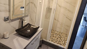 A modern bathroom with a marble vanity, a black sink, a glass shower enclosure, and a marble-tiled shower floor. - Apartment morteau center (Morteau)