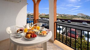 Varanda com mesa posta para o café da manhã, com vista para um estacionamento e prédios.