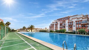 Uma piscina com deck verde, rodeada por edifícios altos com varandas.
