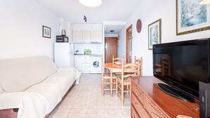 Um espaço de estar compacto com sofá, mesa de jantar com cadeiras, televisão e área de cozinha com máquina de lavar.