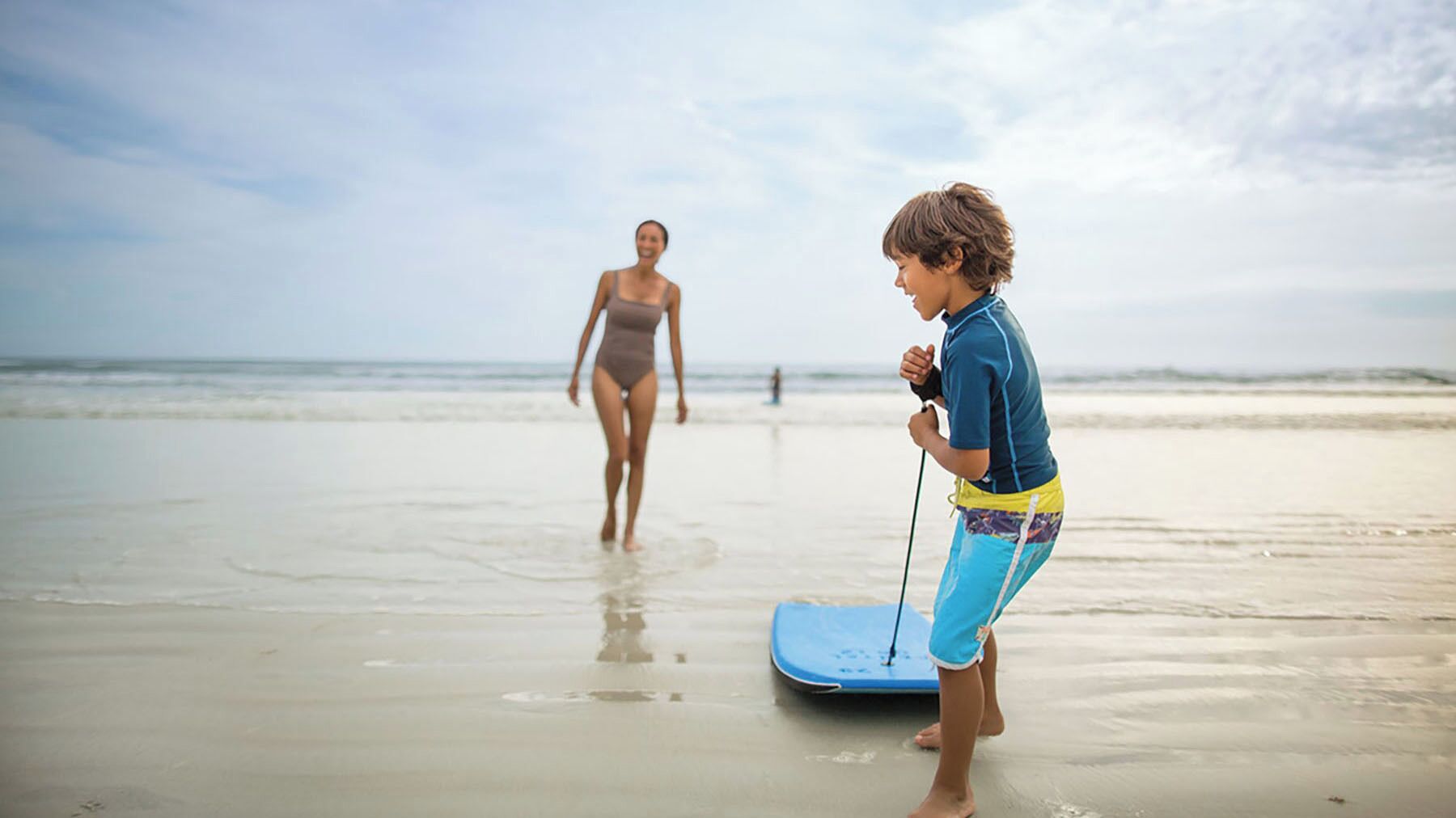 A beach scene with a person in a blue wetsuit and another in a swimsuit.