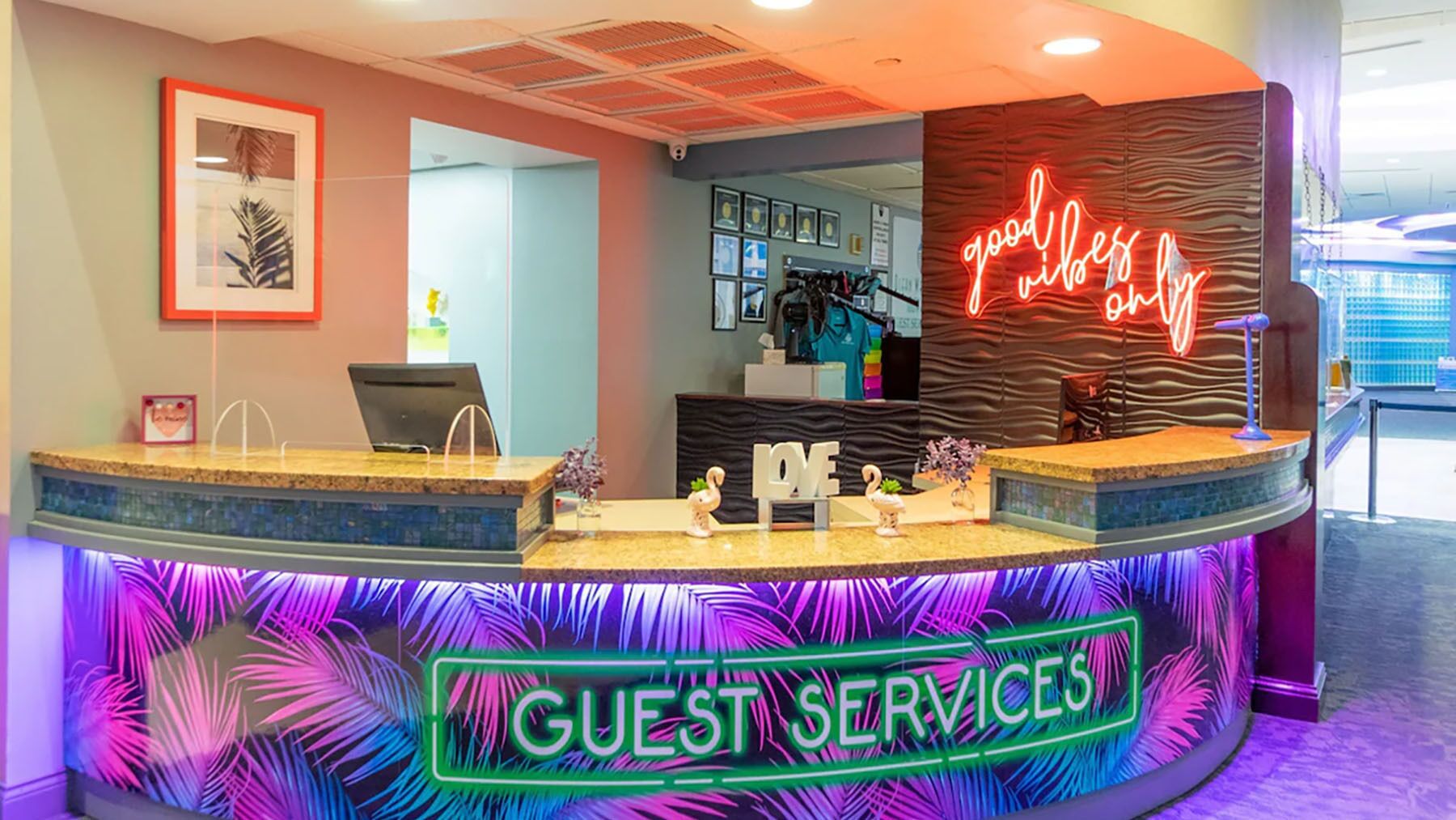 Un área de recepción con un letrero de neón que dice “GUEST SERVICES” y otro letrero de neón que dice “good vibes” encima.